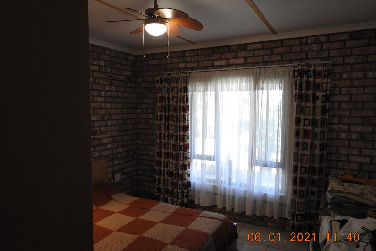 A bedroom featuring exposed brick walls, tiled flooring, and a ceiling fan.