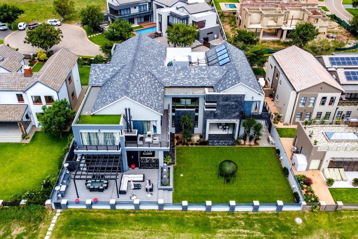 Aerial view of a modern residential property featuring a tiled roof, solar panels, a spacious rear patio with pergola, and a well-maintained garden.