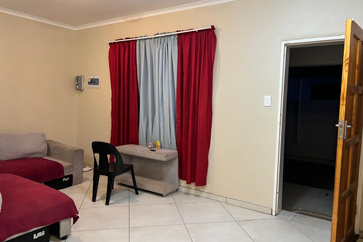 A living room featuring tiled flooring, a wooden door, and a window covered by curtains.