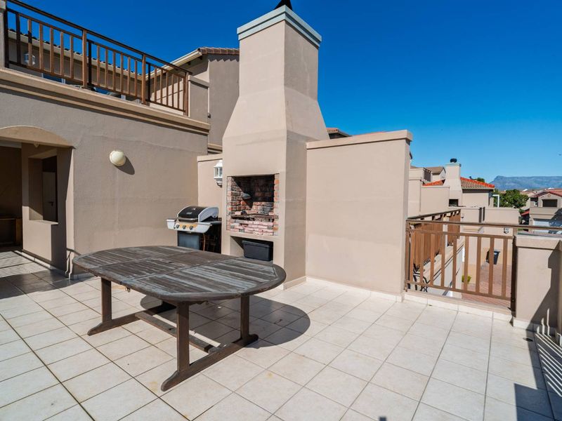 Spacious upper-level balcony featuring a built-in braai, tiled flooring, and protective railings, offering an ideal space for outdoor entertaining.