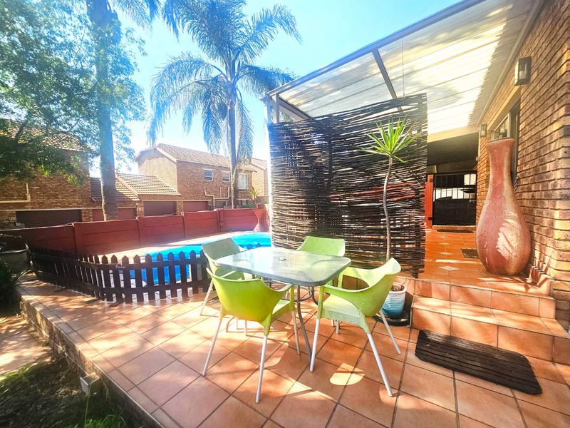 A tiled outdoor patio area featuring a covered roof, adjacent to a swimming pool and brick townhouse exterior.