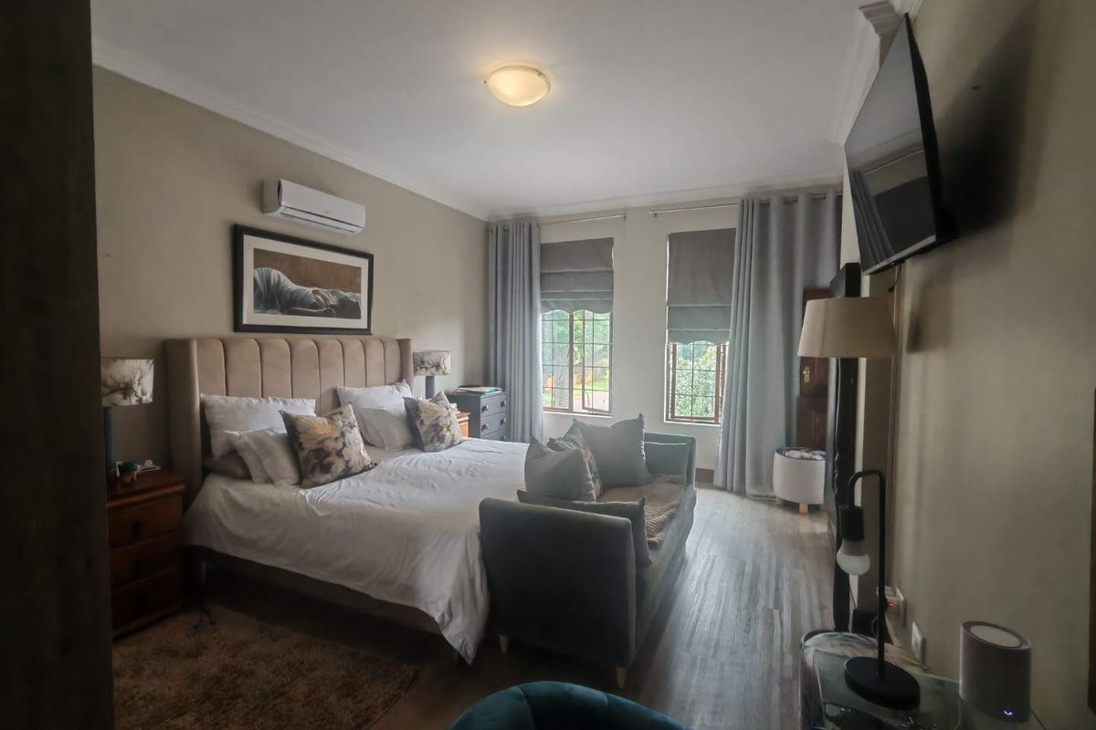 A well-maintained bedroom featuring wood-look flooring, crown molding, dual windows with fitted blinds, and a wall-mounted air conditioning unit.