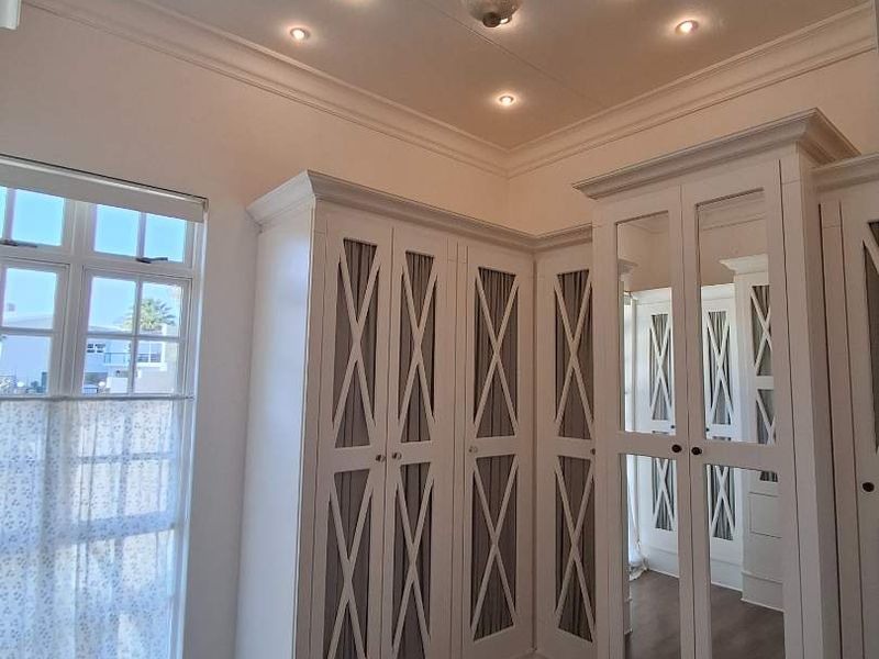 A bright bedroom featuring extensive built-in cabinetry with mirrored doors, decorative ceiling detailing, recessed lighting, and modern laminate flooring.