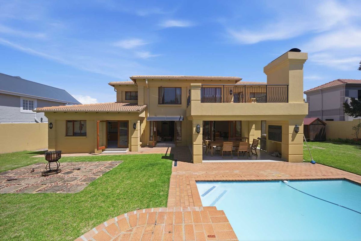Rear view of the property featuring a swimming pool, paved patio area, upper balcony, and a well-maintained garden with a brick boundary wall.
