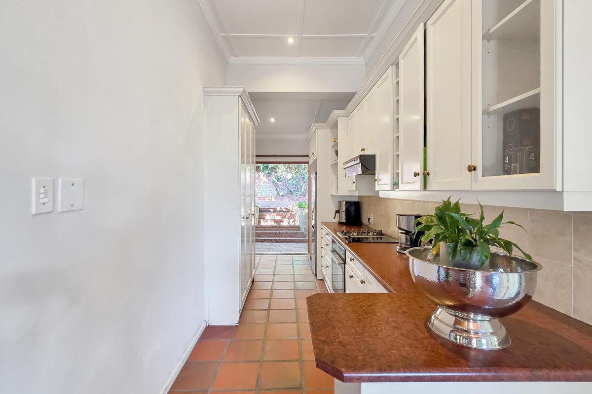 A galley-style kitchen featuring white cabinetry, a gas hob, built-in oven, and terracotta tiled flooring, leading directly to an outdoor patio area.