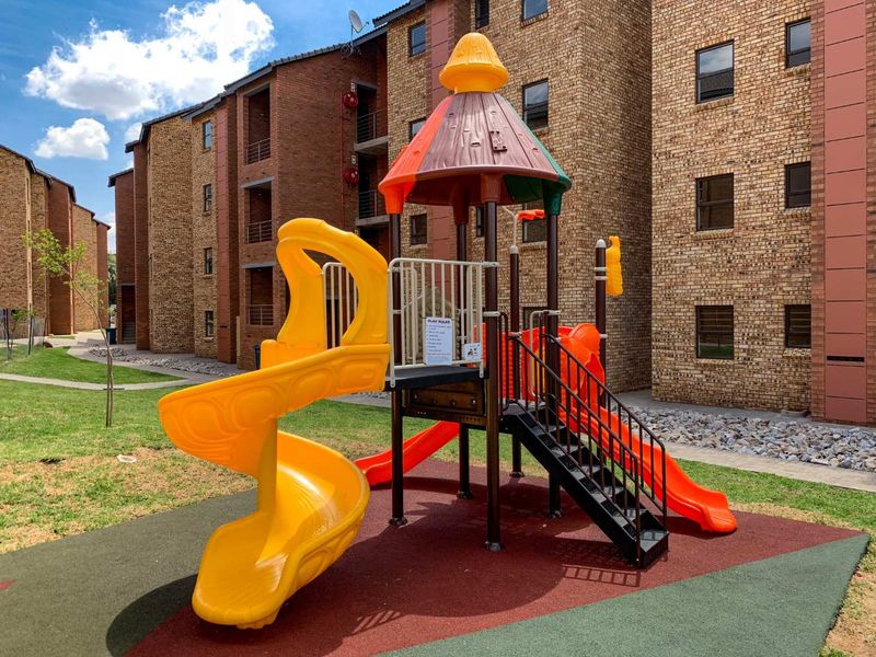 Communal playground area situated between face brick apartment blocks, featuring modern play equipment and well-maintained landscaped grounds.