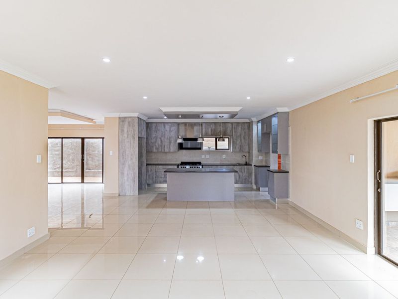 Spacious open-plan living area featuring a modern kitchen with a central island, sleek cabinetry, and large tiled floors, leading to an outdoor patio space.