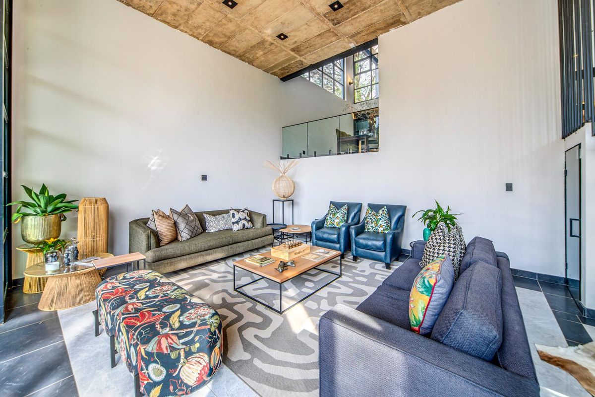 Spacious living room featuring a dramatic double-volume height, exposed concrete ceiling, and large windows that provide abundant natural light.