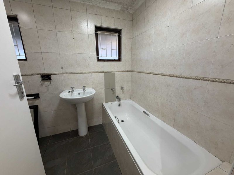 A dated bathroom featuring a pedestal basin, built-in bathtub, and full-height wall tiling. The space requires cosmetic updates to modernize the finishes.