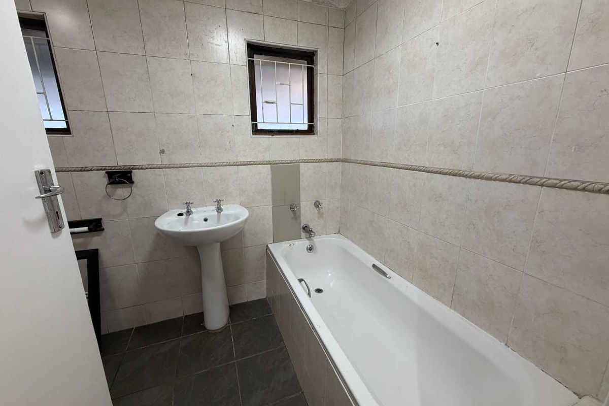 A dated bathroom featuring a pedestal basin, built-in bathtub, and full-height wall tiling. The space requires cosmetic updates to modernize the finishes.