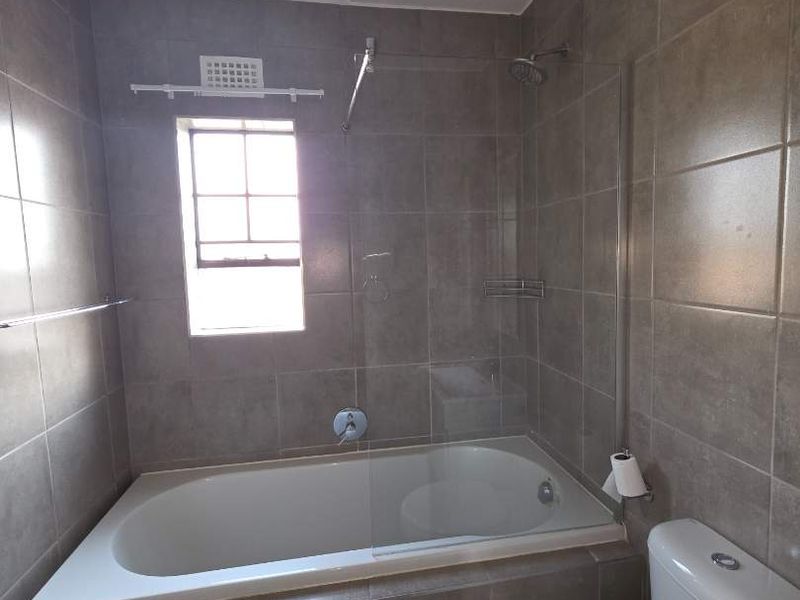 A clean, modern bathroom featuring a built-in bathtub with a glass shower screen, tiled walls, and a standard ceramic toilet.