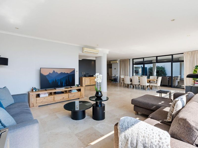 Spacious open-plan living and dining area featuring polished travertine flooring, recessed lighting, and large sliding glass doors leading to an outdoor patio.