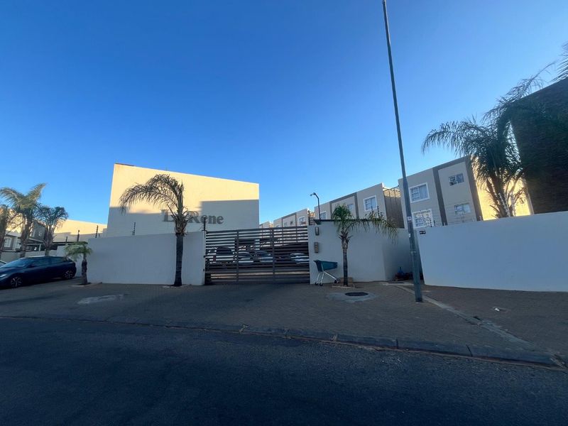 Front elevation of the Le Rene apartment complex featuring a secure gated entrance, perimeter wall with electric fencing, and paved driveway access.