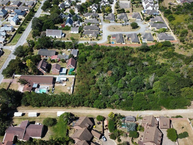 An aerial view of a vacant residential plot surrounded by established suburban housing and dense natural vegetation.