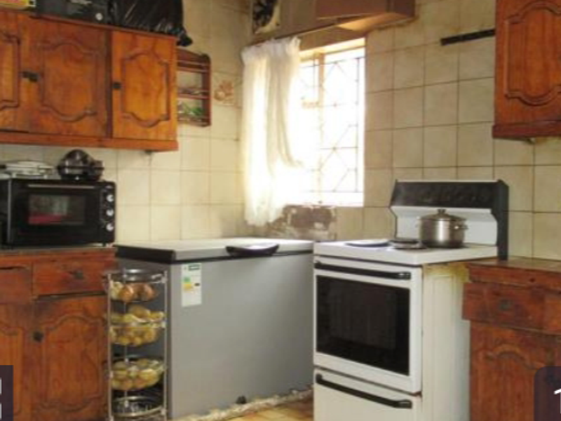 A dated kitchen featuring traditional wooden cabinetry, tiled wall surfaces, and a freestanding stove, offering significant potential for a modern renovation.