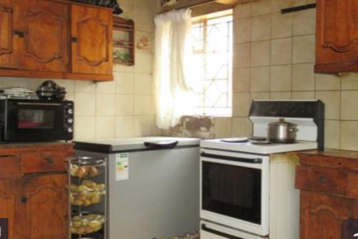 A dated kitchen featuring traditional wooden cabinetry, tiled wall surfaces, and a freestanding stove, offering significant potential for a modern renovation.