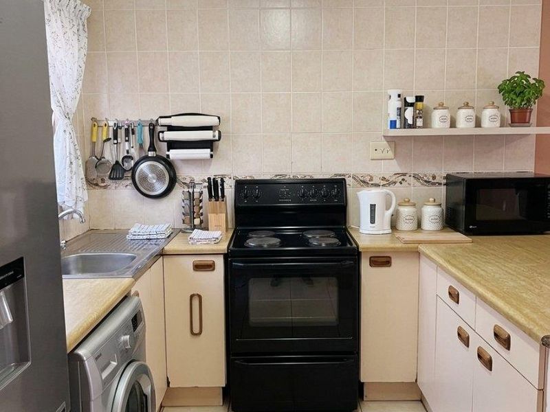 A functional kitchen featuring laminate countertops, ceramic tile backsplash, tiled flooring, and a freestanding electric stove with integrated cabinetry.