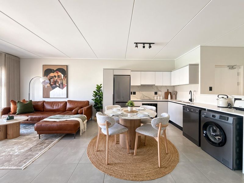 Modern open-plan living area featuring a sleek kitchen with stone countertops, integrated appliances, and tiled flooring, seamlessly flowing into a comfortable lounge space.