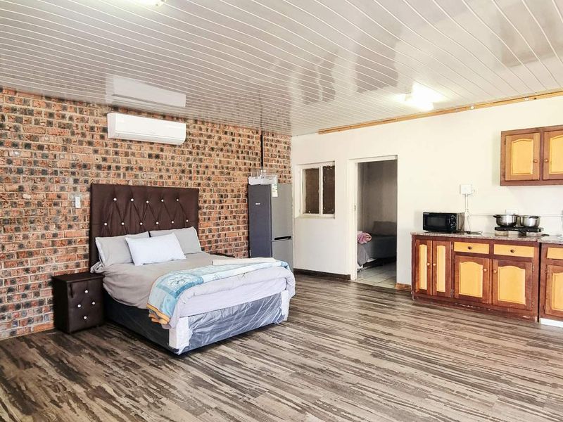 Open-plan studio space featuring an exposed brick feature wall, laminate flooring, and a functional kitchenette with built-in cabinetry.