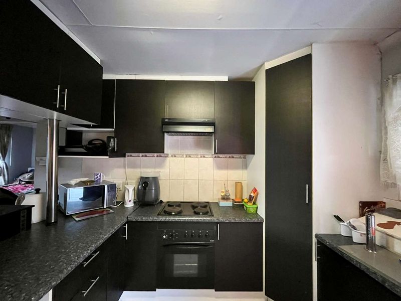 Compact kitchen featuring dark cabinetry, laminate countertops, built-in oven, electric hob, and an integrated extractor fan with tiled backsplash.