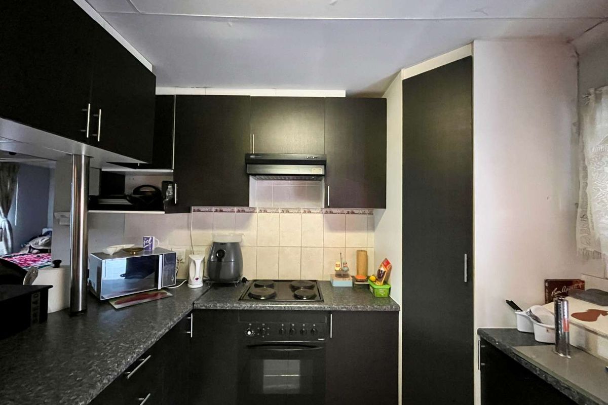 Compact kitchen featuring dark cabinetry, laminate countertops, built-in oven, electric hob, and an integrated extractor fan with tiled backsplash.