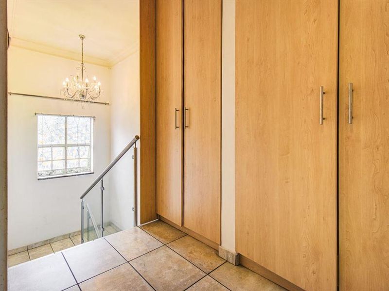 A bright hallway featuring tiled flooring, ample built-in cupboard storage, and a staircase with a modern glass balustrade.