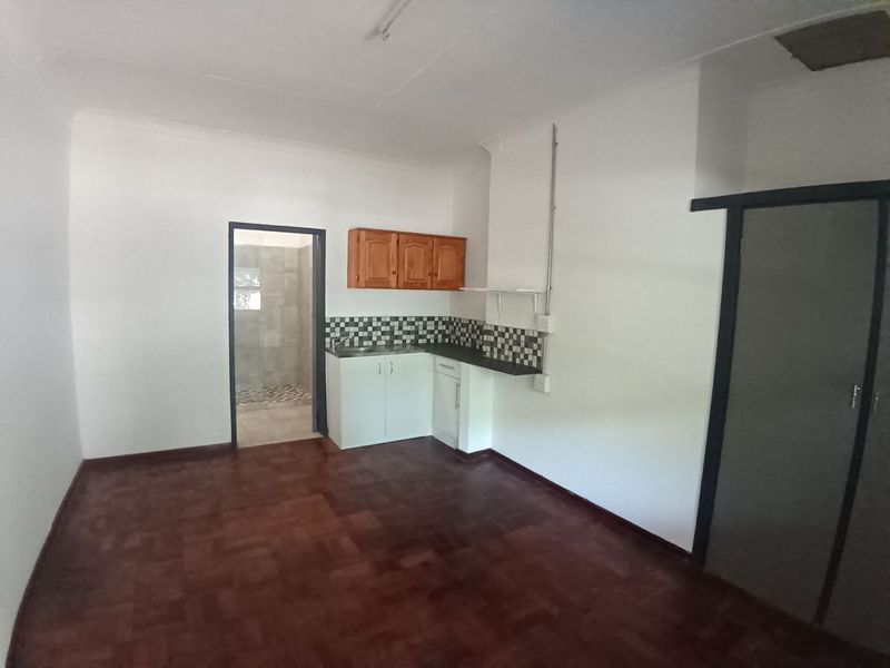 A compact kitchen area featuring basic cabinetry, a tiled backsplash, and parquet flooring, with an adjacent bathroom visible through the doorway.