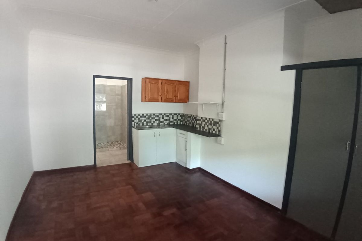 A compact kitchen area featuring basic cabinetry, a tiled backsplash, and parquet flooring, with an adjacent bathroom visible through the doorway.