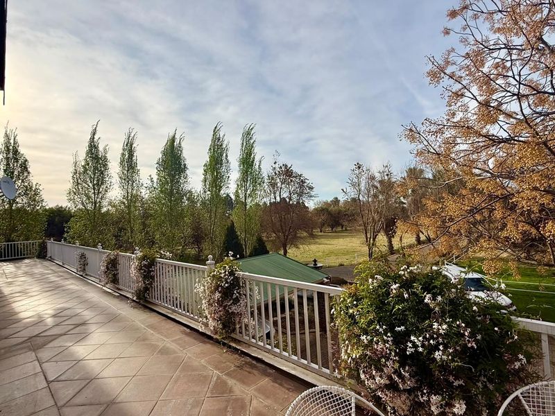 A spacious elevated balcony featuring tiled flooring and a white metal balustrade, offering scenic views over the surrounding small holding grounds.