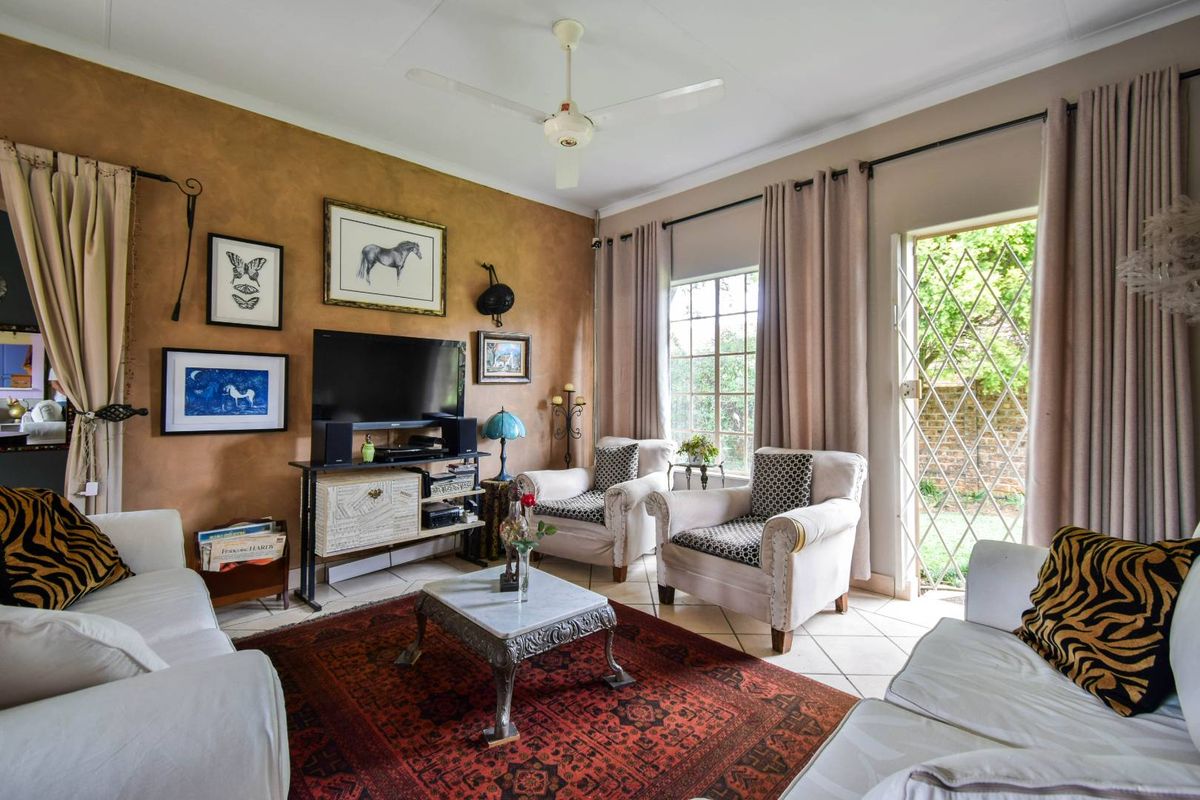 A comfortable living room featuring tiled flooring, a ceiling fan, and a glass-paned door providing direct access to the garden area.