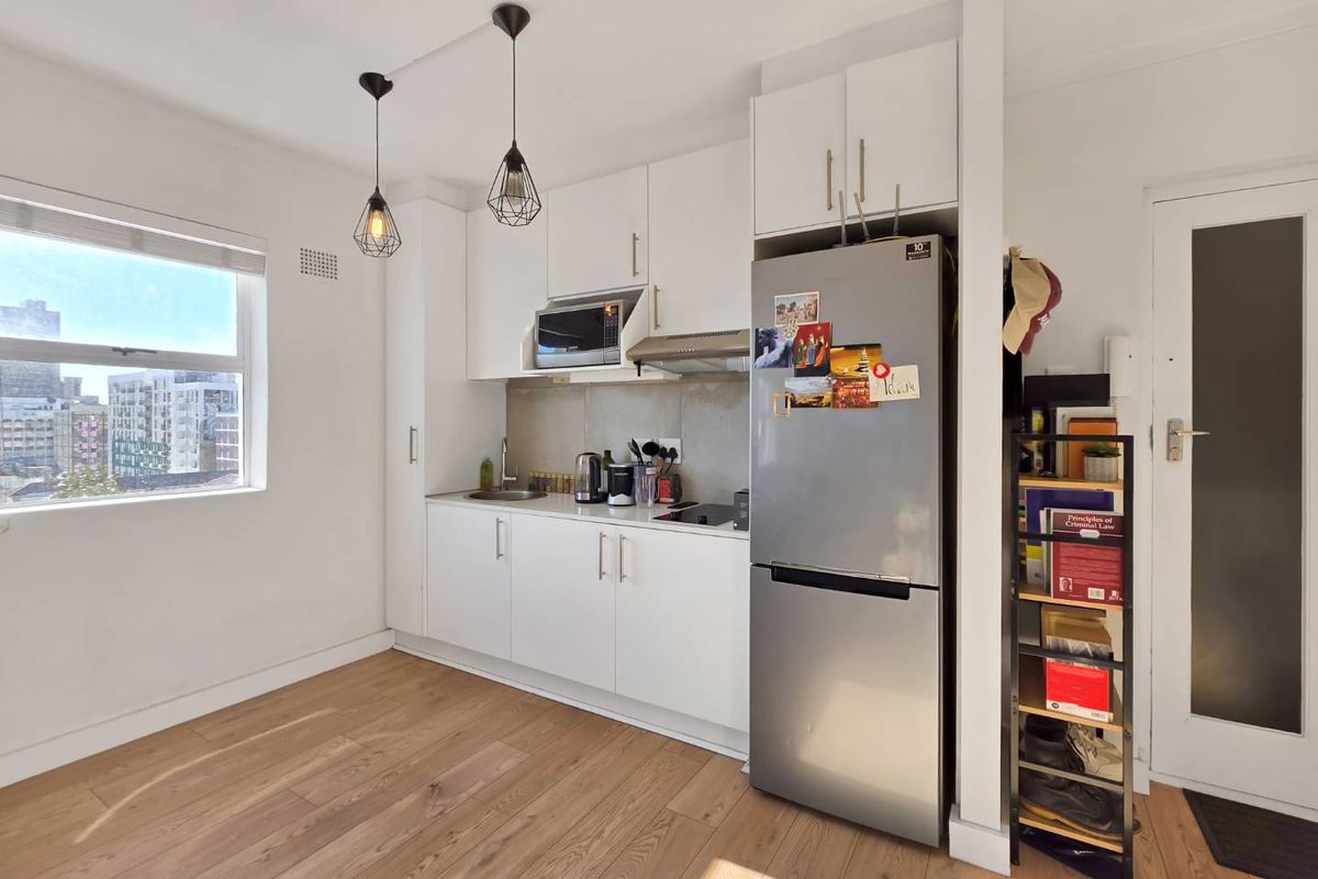 Compact modern kitchen featuring white cabinetry, integrated appliances, laminate flooring, and pendant lighting, offering a clean and functional culinary space.