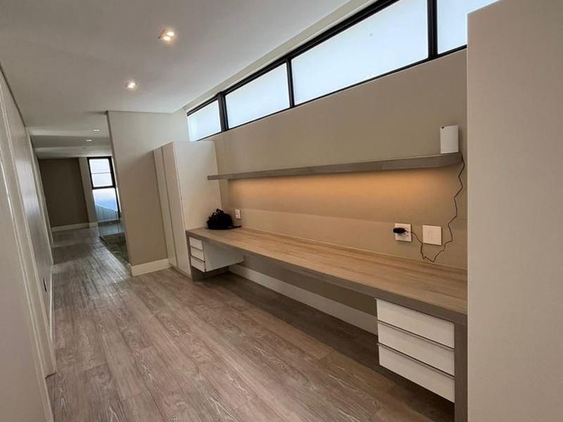 A modern, minimalist home office space featuring a long built-in desk, integrated shelving, recessed lighting, and clerestory windows for natural light.