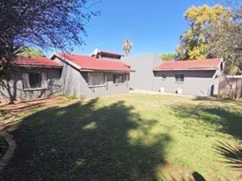 A view of the rear exterior of the house featuring a spacious lawn, metal roofing, and secure window treatments.