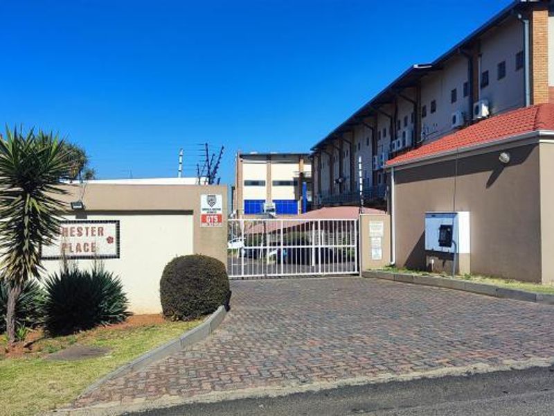 Front entrance view of Chester Place townhouse complex featuring a secure gated access point, paved driveway, and perimeter security fencing.