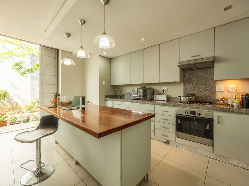 Modern kitchen featuring a central island with a wooden countertop, granite surfaces, built-in oven, gas hob, and direct access to an outdoor patio area.