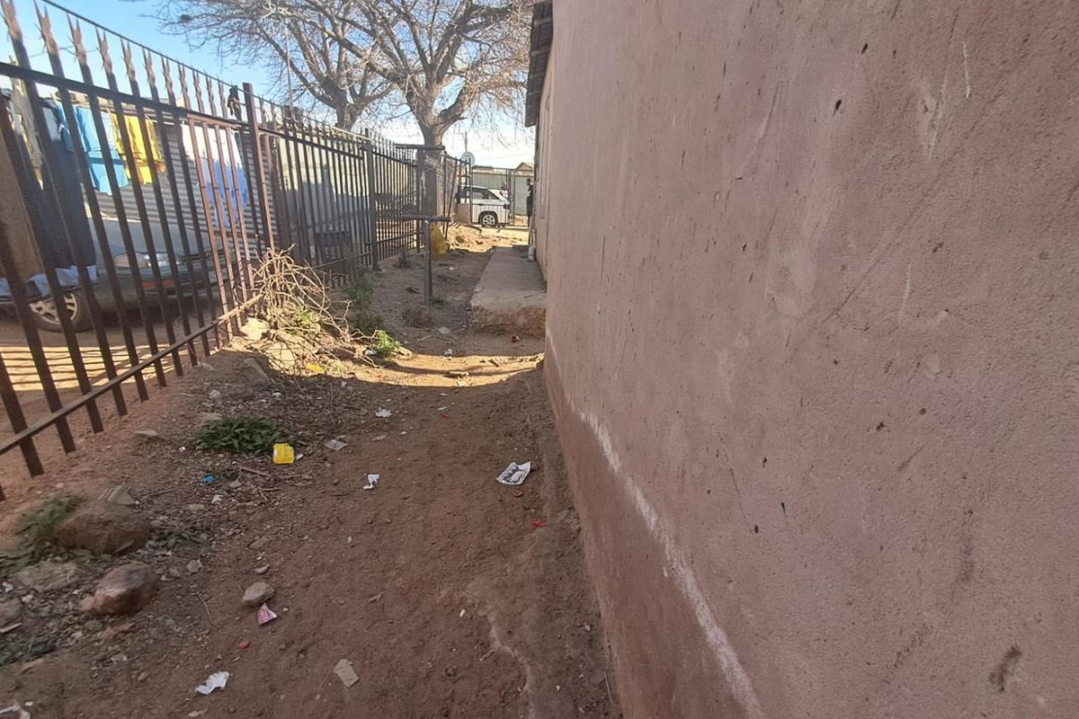 A narrow side passage along the exterior of the house featuring a plastered wall and metal perimeter fencing.