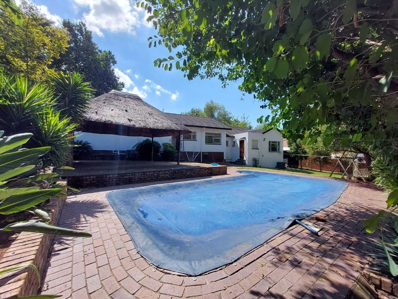 Outdoor entertainment area featuring a swimming pool with a cover and a traditional thatch lapa set within a paved garden space.