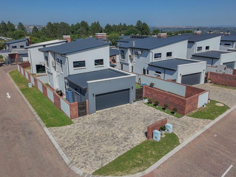 Aerial view of a modern residential property featuring a paved driveway, brick boundary walls, and a double garage within a secure estate.