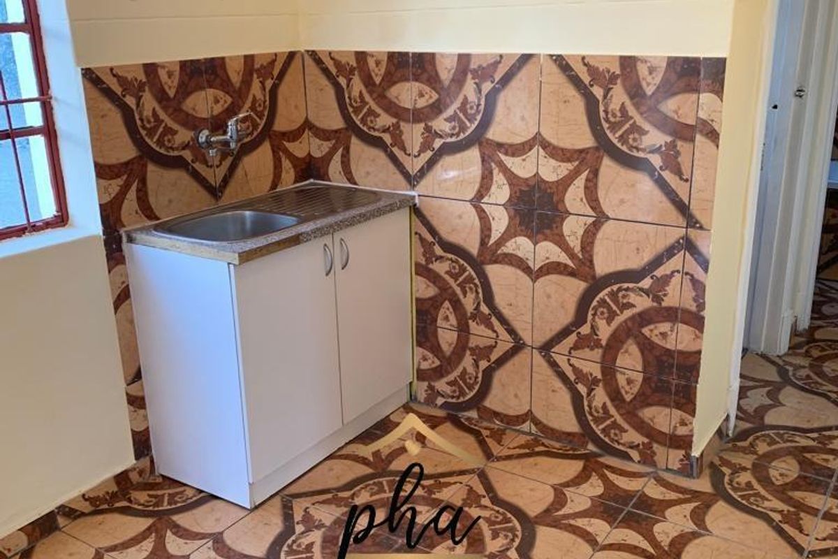 A compact kitchen area featuring a single sink unit, tiled splashbacks, and patterned floor tiles throughout the space.