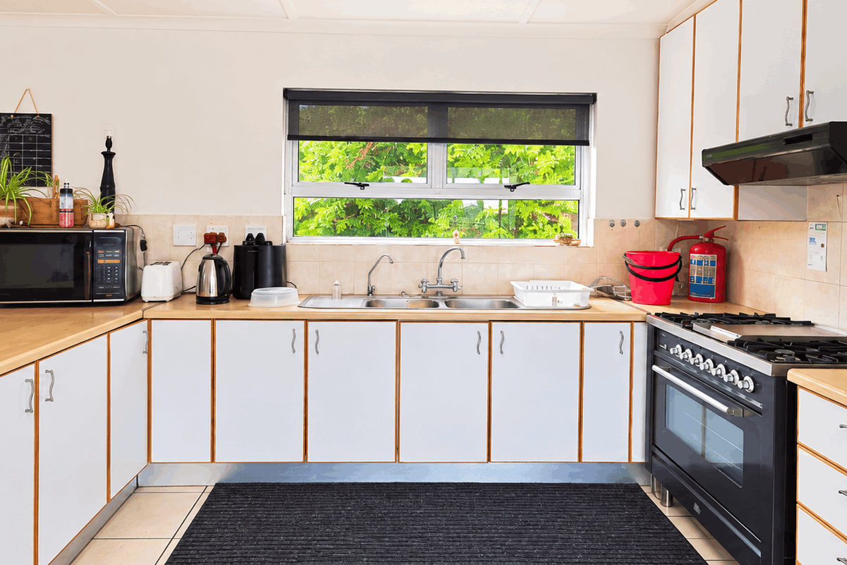 A functional kitchen featuring white cabinetry, laminate countertops, a double sink, and a built-in gas stove with an extractor fan.