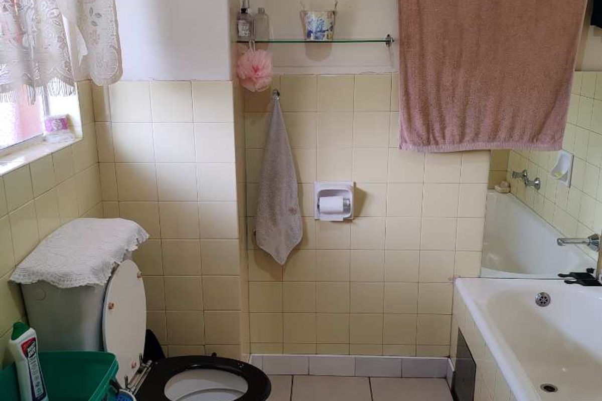 A dated bathroom featuring a standard bathtub, toilet, and tiled walls with visible wear, offering a functional space ready for modernization.