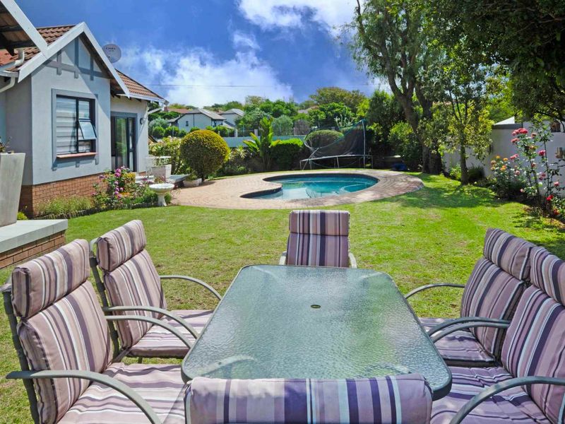 A well-maintained rear garden featuring a swimming pool with brick paving, lush lawn, and established landscaping, viewed from the patio area.