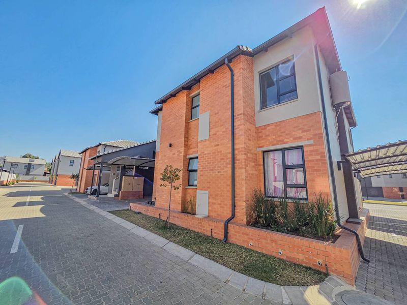A modern double-storey townhouse featuring a face brick facade, aluminium window frames, and a paved driveway with an integrated carport.