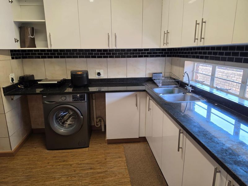 A functional kitchen featuring white cabinetry, dark granite countertops, a double sink, and a subway tile backsplash with integrated laundry plumbing.