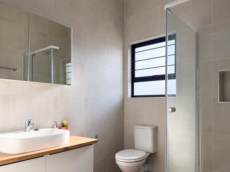 A modern, well-maintained bathroom featuring neutral wall tiles, a vessel sink vanity, a glass-enclosed shower with a recessed niche, and a toilet.