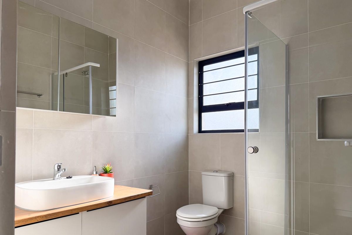A modern, well-maintained bathroom featuring neutral wall tiles, a vessel sink vanity, a glass-enclosed shower with a recessed niche, and a toilet.