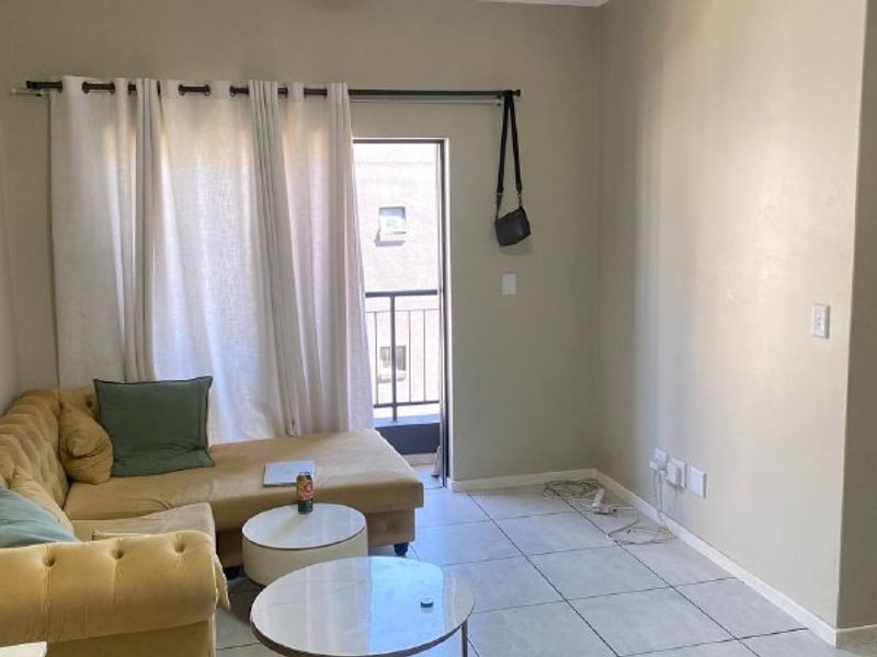 A living room area featuring tiled flooring and direct access to a balcony through a sliding door.
