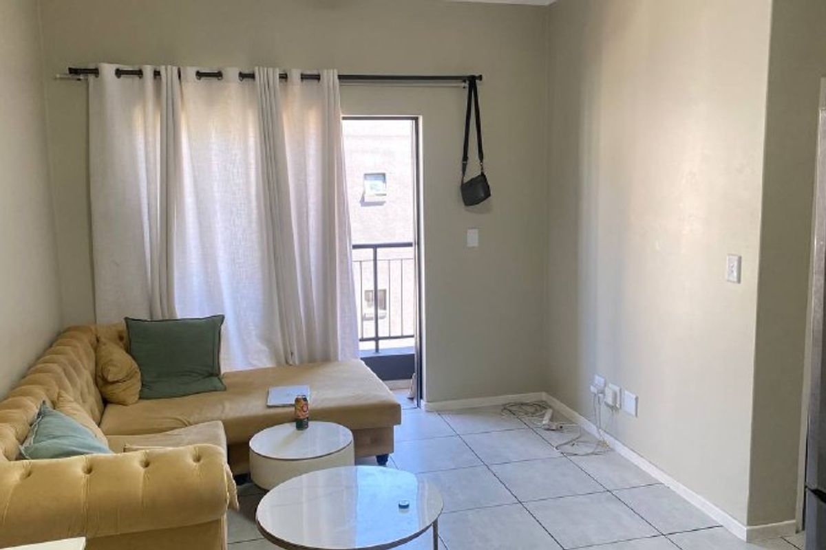 A living room area featuring tiled flooring and direct access to a balcony through a sliding door.
