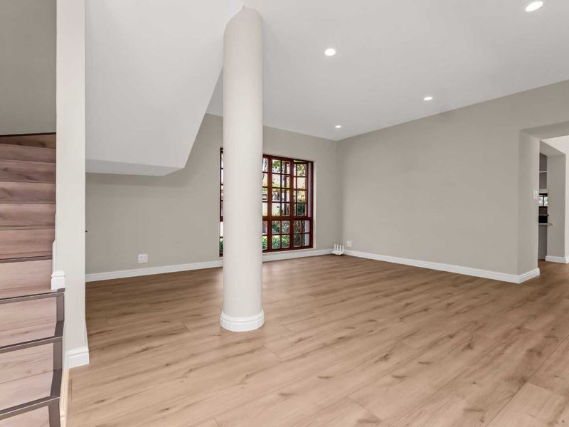 A bright, open-plan living area featuring modern laminate flooring, a central structural column, and a staircase leading to the upper level.