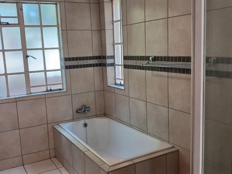 A functional bathroom featuring a built-in bathtub, separate shower enclosure, and neutral wall tiling with a decorative border.